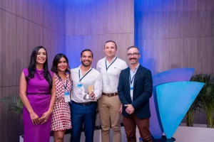 Dos mujeres y 3 hombres, uno de los hombre sostiene un premio AVA.