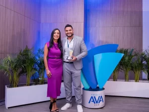 Una mujer y un hombre posando, el hombre sostiene un premio AVA.